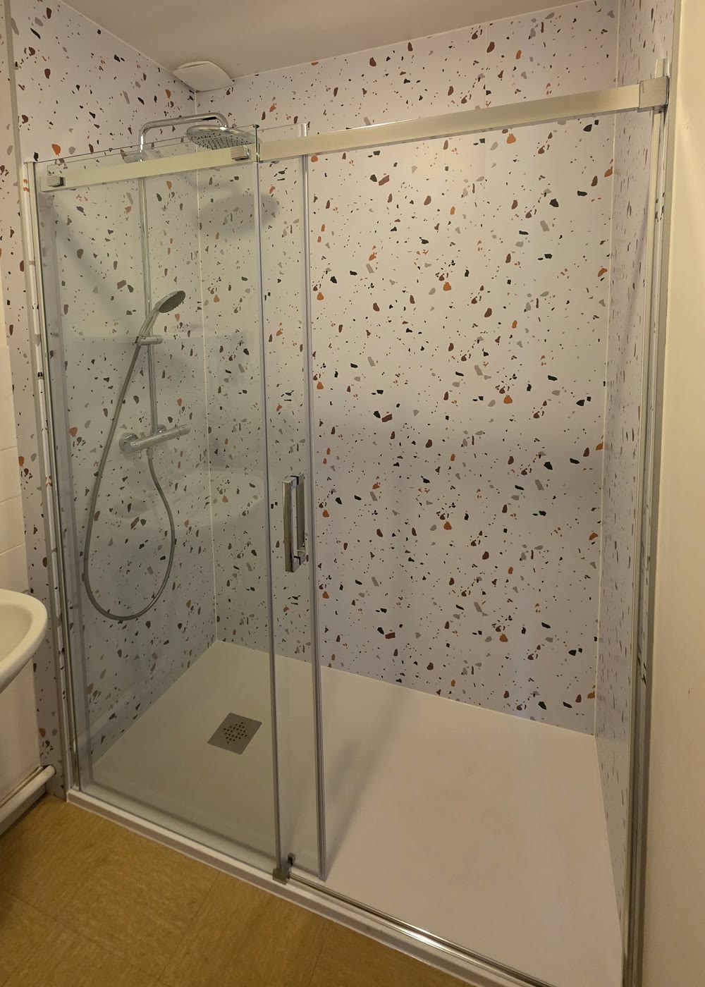 Après — grande douche avec paroi vitrée coulissante et murs effet terrazzo, installée par T'Eau Services à la place de la baignoire